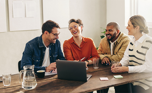 four employees sitting at a table at work and laughing